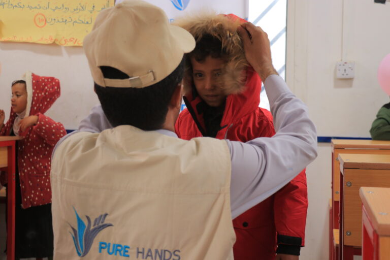 A Pure Hands team member helps a child put on a warm winter coat in Yemen